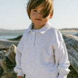Child standing in a natural setting with large logs and a clear sky.