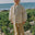 A young child standing on a sandy beach wearing a cream-colored linen jacket and matching wide-leg pants, with green beach plants and the ocean in the background.