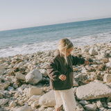Child walking across a rocky beach wearing the Amélie Coat in Cacao brown over a cream outfi