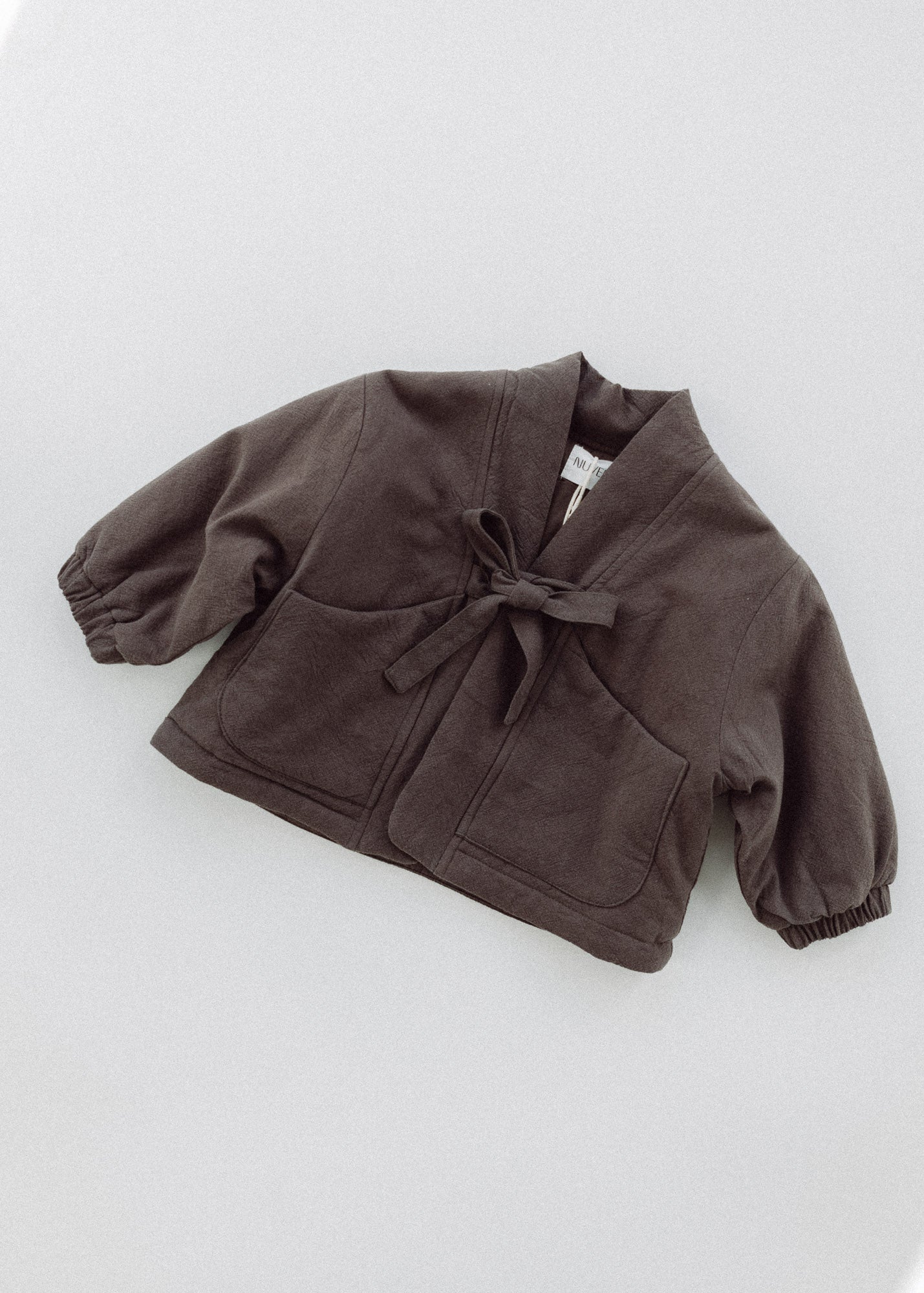 Amélie kids' coat in Cacao brown laid flat, showing the tie front, patch pockets and elasticated cuffs