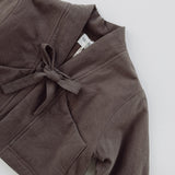 Flat-lay detail of the Amélie Coat in Cacao brown, showing the fabric texture, front bow and patch pocket