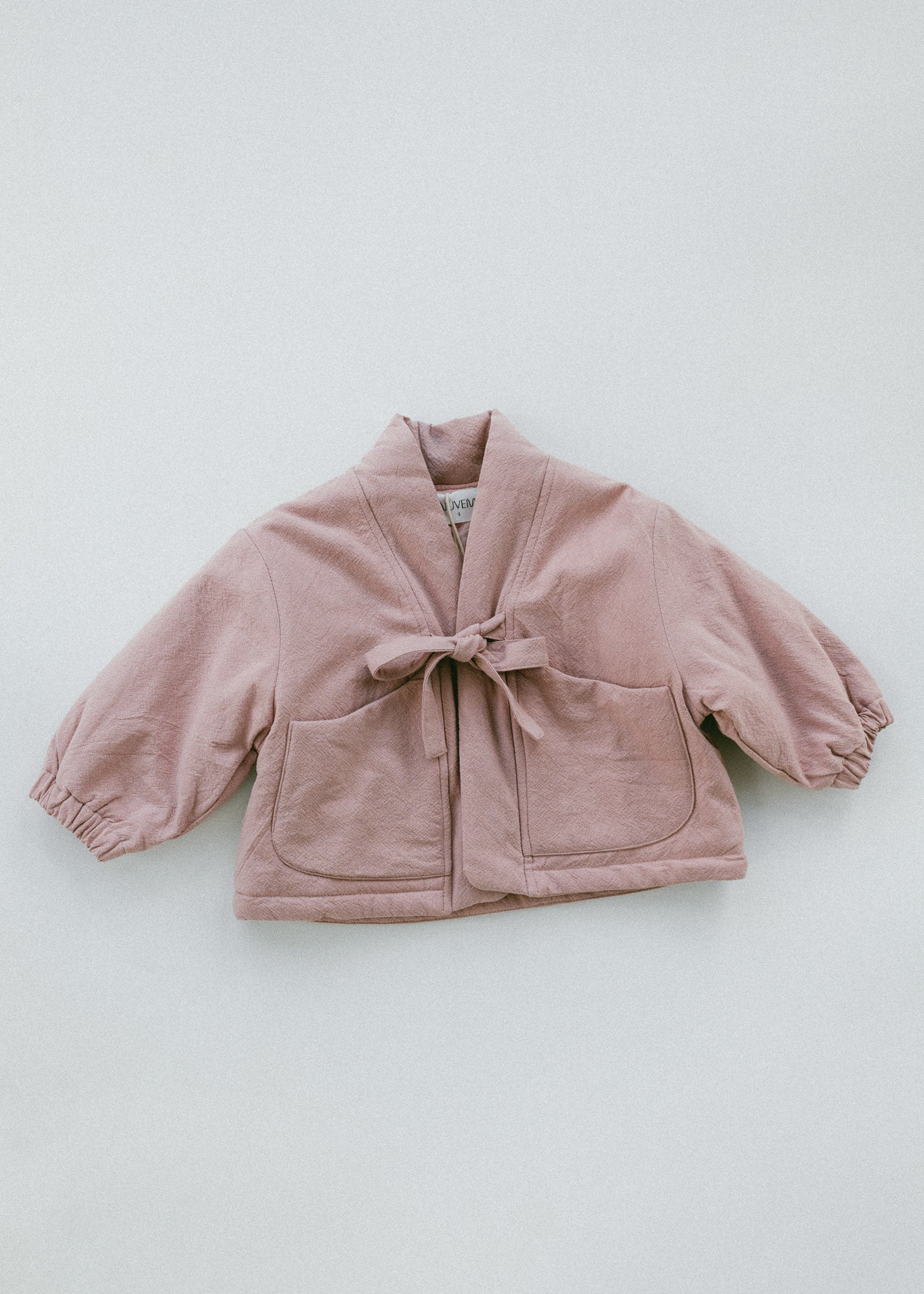 A dusty pink cropped jacket with a tie-front closure and front patch pockets, laid flat on a light gray background.